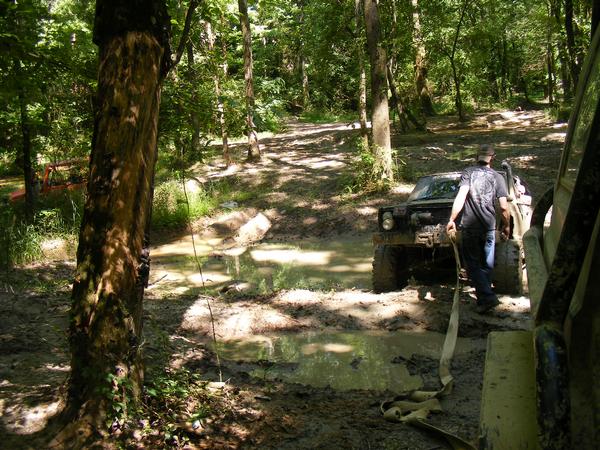Off-road vehicles stuck in mud on a forest trail, one vehicle being pulled by a strap