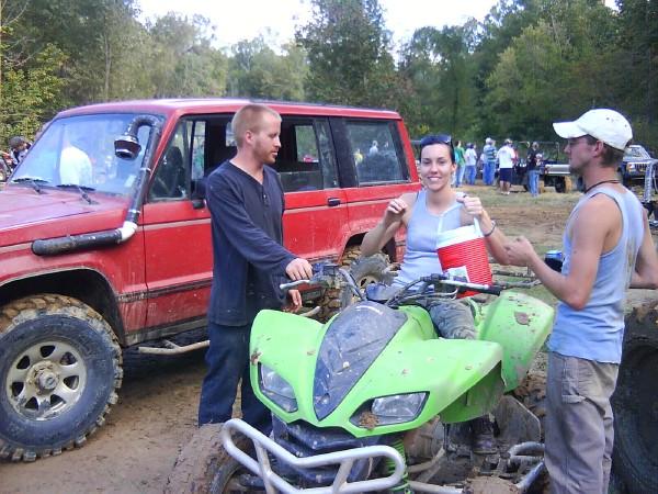 Red SUV with snorkel, green ATV, and three people in muddy outdoor setting