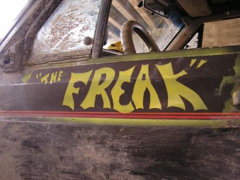 Side view of a dirty off-road vehicle with "THE FREAK" painted in yellow on the door