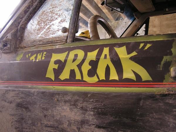 Side view of a dirty off-road vehicle with "THE FREAK" painted in yellow on the door