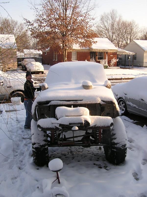 Person standing next to a heavily snow-covered off-road vehicle with large tires