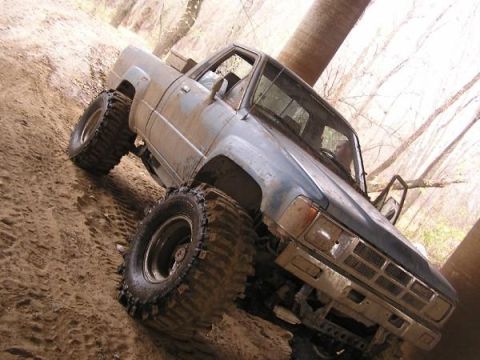 Muddy blue pickup truck with oversized tires on a dirt trail