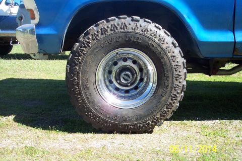 1978 Ford Bronco - A close-up view of a large, aggressive off-road tire mounted on a shiny rim, attached to a blue vehicle.