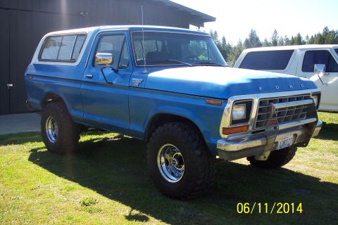 1978 Ford Bronco - A blue 1978 Ford Bronco is parked on a grassy area next to a building, with another vehicle visible behind it.