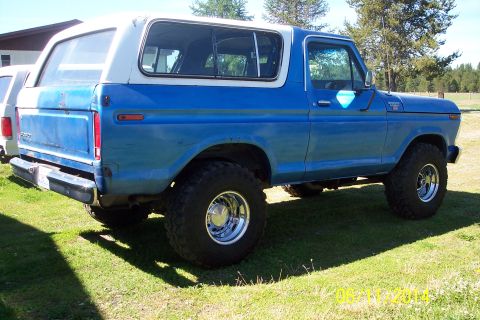 1978 Ford Bronco - A blue and white 1978 Ford Bronco is parked on a grassy lawn, showing its large tires and classic body style.