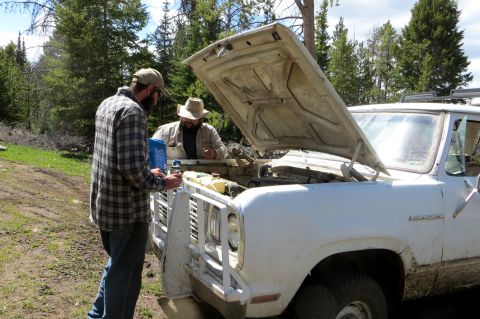 1989 Ford Bronco - Two men attend to the engine of a white pickup truck in a wooded area.