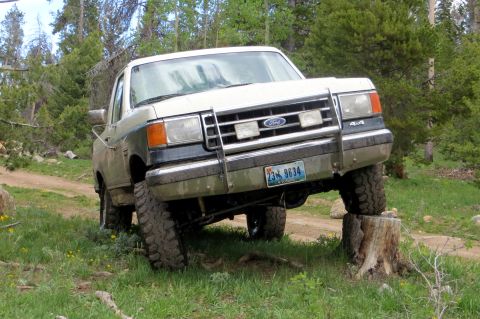 1989 Ford Bronco - Ford Bronco navigates an obstacle on a dirt road, with one front wheel elevated on a tree stump.