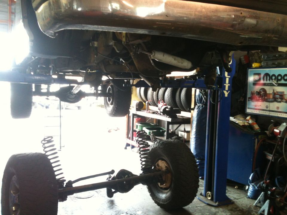 Truck chassis on a blue lift, showing suspension and undercarriage. The front axle is removed