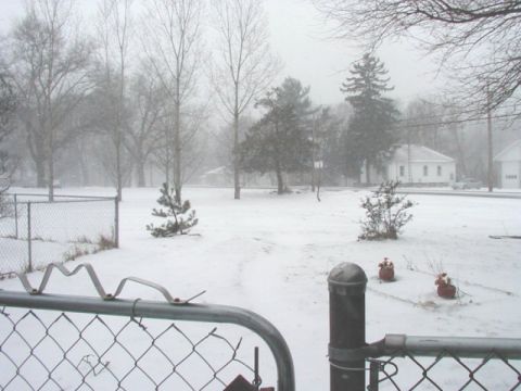 1997 Ford Taurus - A snowy scene with a chain-link fence in the foreground and a car visible in the distance.
