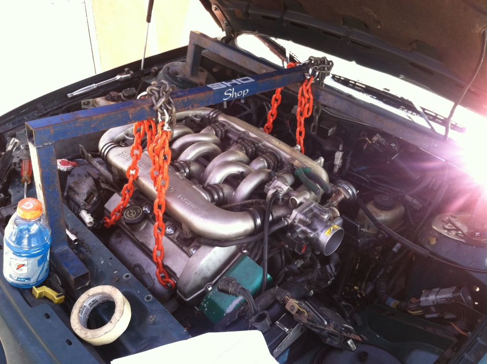 engine hoist supporting a V6 engine being removed from a car. A bottle of Gatorade and tape are on the fender