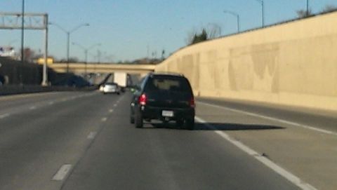 2000 Mercury Grand Marquis - A black SUV is seen from behind on a highway with a concrete barrier on the right.