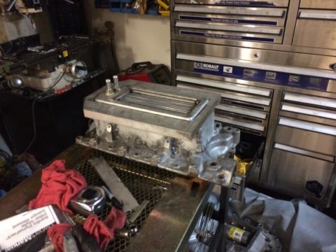 1996 Ford Bronco - Supercharger intake manifold sits on a metal grate next to tools and rags in a workshop.