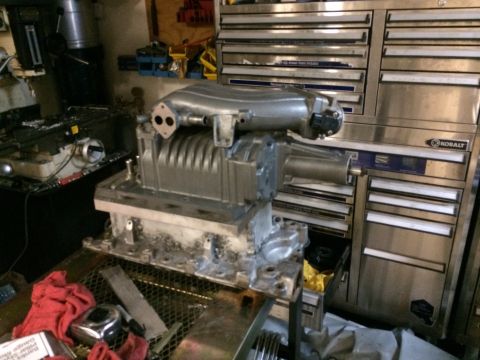 1996 Ford Bronco - A supercharger assembly sits on a workbench in a garage setting.