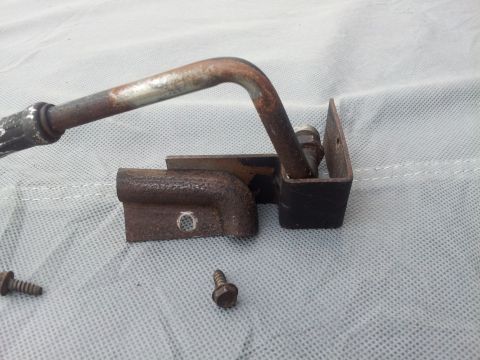 1976 Ford Ranchero - A close-up view of a rusted metal lever mechanism, including two screws, resting on a textured fabric surface.