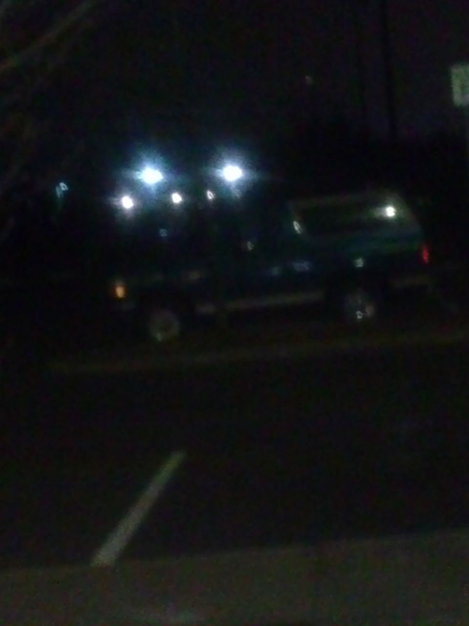 Dark SUV parked at night, illuminated by overhead lights