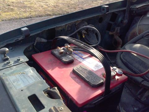 1996 Ford Bronco - Close-up view of a car's engine bay, focusing on a red battery and associated wiring.