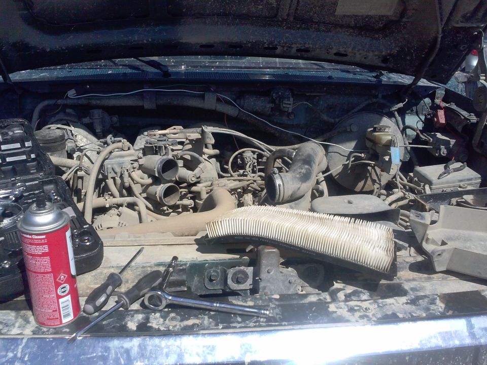 Engine bay with tools and a removed air filter. A can of cleaner is on the left