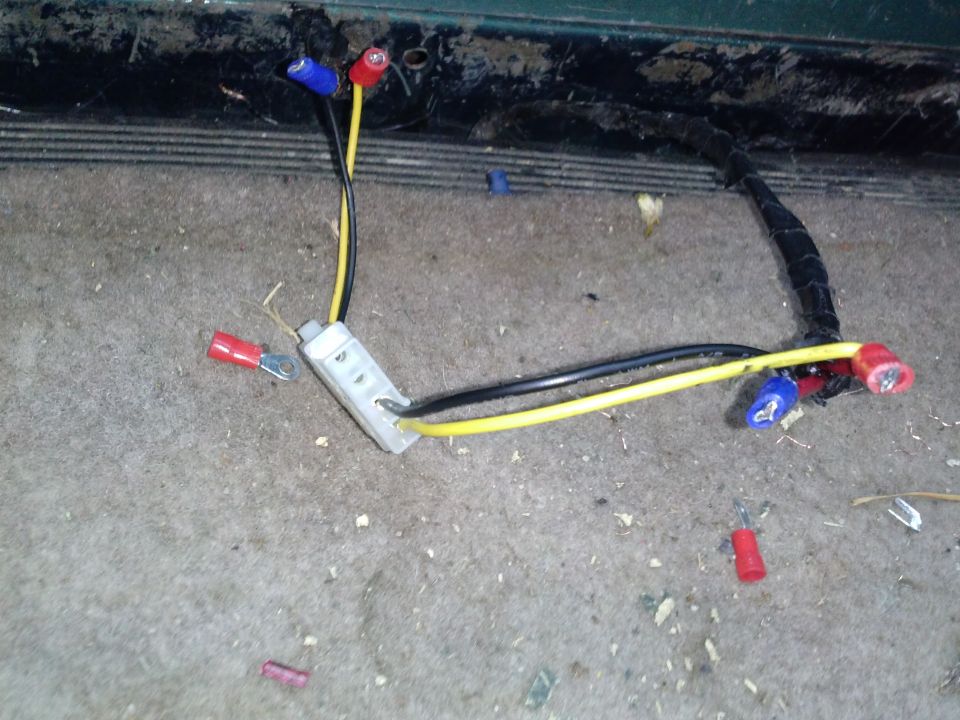 Vehicle wiring harness with yellow and black wires, connectors, and a gray junction block on carpeted floor