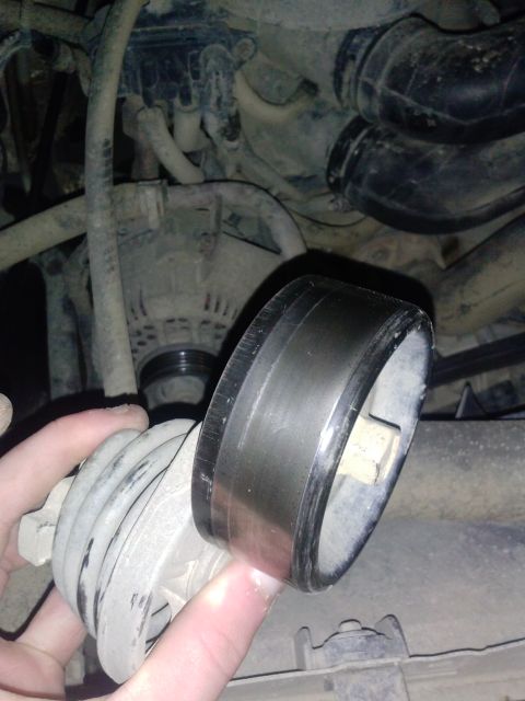 1996 Ford Bronco - A close-up view of a vehicle's engine belt tensioner pulley being held by a hand.
