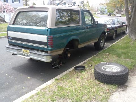 1996 Ford Bronco - Changing a flat tire on a 1996 Ford Bronco parked on the side of the road.