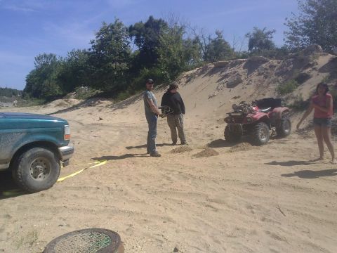 1996 Ford Bronco - A green pickup truck and a red ATV are parked in a sandy area with people around.