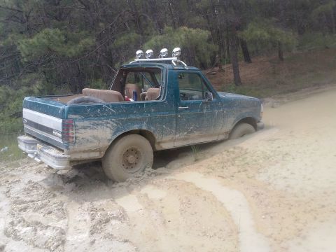 1996 Ford Bronco - A green Ford Bronco is stuck in mud on a wooded trail.