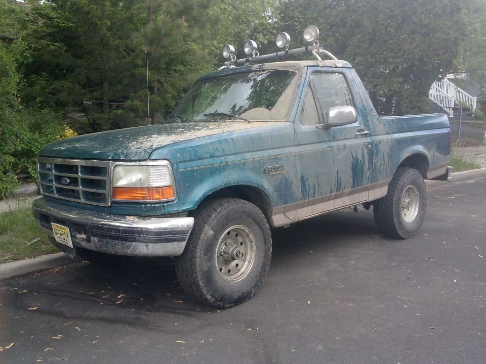 Teal Ford Bronco with roof-mounted lights and aftermarket wheels, covered in dirt