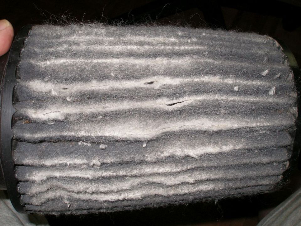 Dirty air filter with white debris accumulated on dark gray filter media