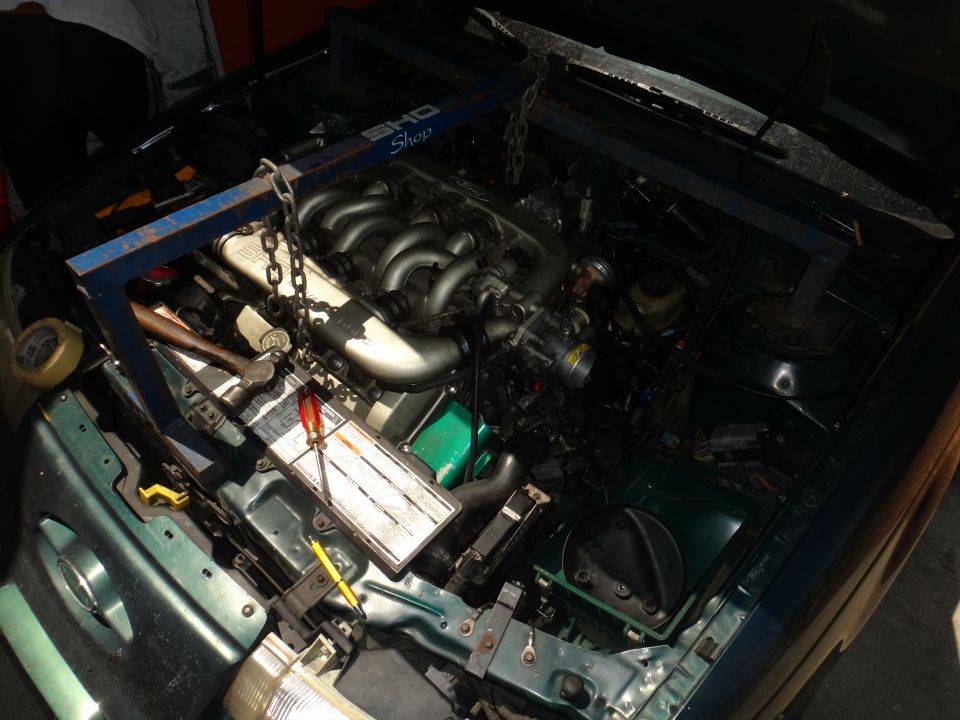 Engine bay with engine hoist over the motor. Tools like a screwdriver and hammer are on a white panel