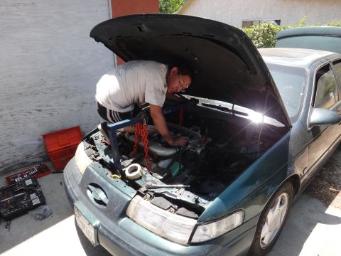 1993 Ford Taurus - A mechanic works on the engine of a green 1993 Ford Taurus, with tools laid out nearby.
