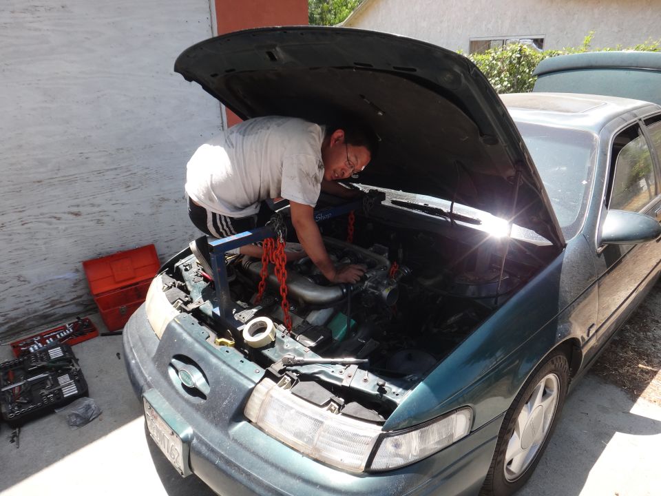 Green 1993 Ford Taurus with hood open, man working on engine
