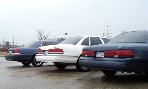 1998 Ford Crown Victoria - Three Ford Crown Victorias are parked in a lot on a cloudy day.