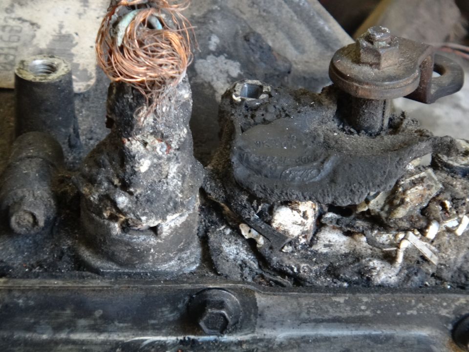 Close-up of a heavily corroded electrical connection with frayed copper wires and black buildup