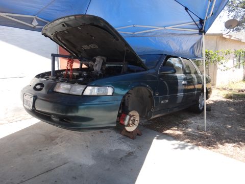 1993 Ford Taurus - Green 1993 Ford Taurus sedan undergoing maintenance with the hood open and front wheel detached.