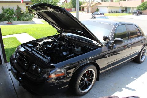 2003 Ford Crown Victoria - black full-size four-door sedan sits in a residential driveway with its hood raised, exposing the engine bay.