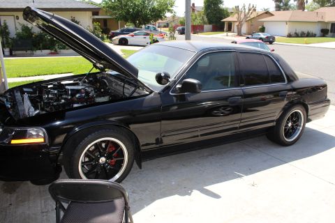 2003 Ford Crown Victoria - Side view of a lowered black four-door sedan in a driveway, hood raised, riding on black wheels with red brake calipers.