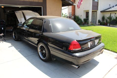 2003 Ford Crown Victoria - Rear three-quarter view of a lowered black four-door sedan with dual exhaust and black wheels parked in a driveway.