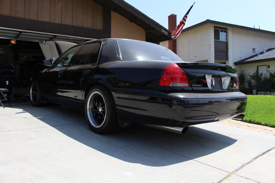 Rear of a black sedan with rear spoiler and dual exhaust in a driveway