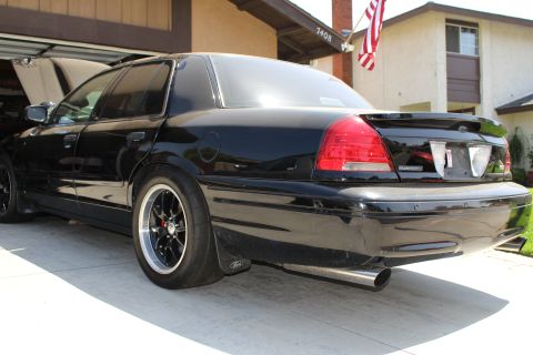 2003 Ford Crown Victoria - Rear quarter of a lowered black sedan on black wheels with rear drag-style tires and a Ford oval on the bumper.