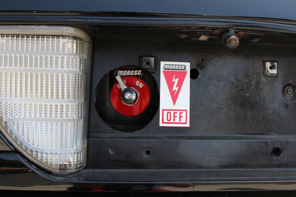 Close-up of a red Moroso battery cut-off switch and on/off decal on a black panel