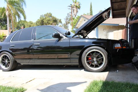 2003 Ford Crown Victoria - Side view of a black sedan in a sunny driveway with hood open; a man stands working at the far right.