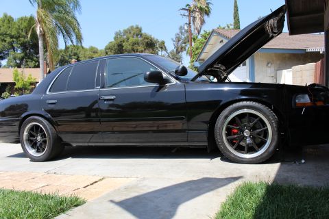 2003 Ford Crown Victoria - Side profile of a lowered black four-door sedan on black wheels with red brakes, hood raised, in a driveway.