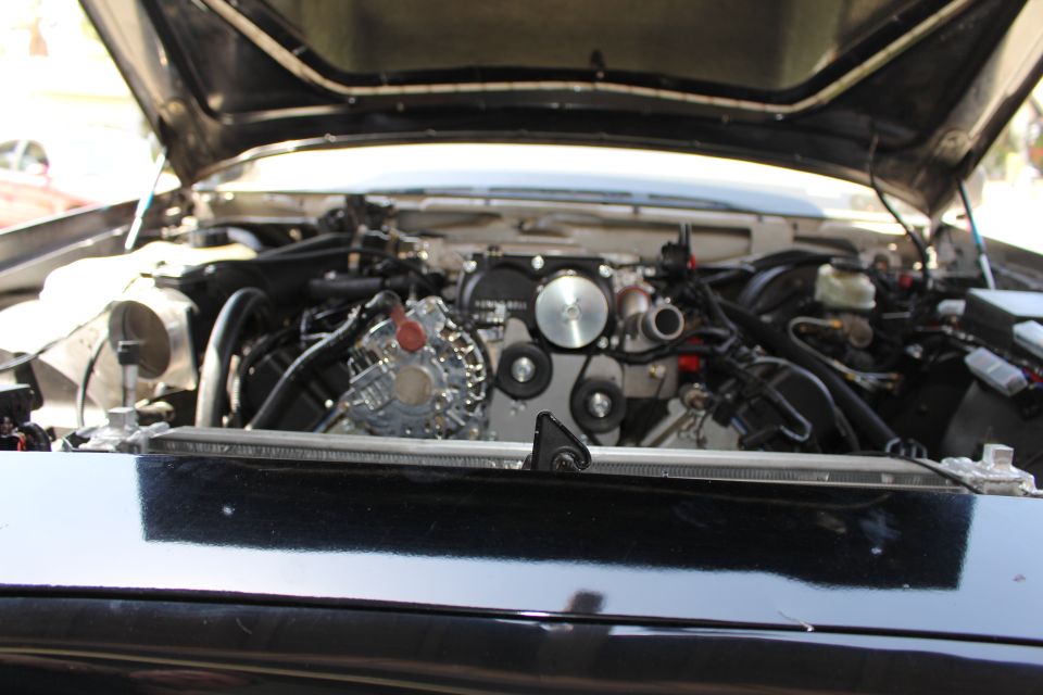 Engine bay viewed across a black front cowl showing a polished pulley assembly