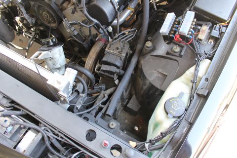 2003 Ford Crown Victoria - partly disassembled engine compartment with a coolant overflow reservoir, fuse box and bundled wiring harnesses.