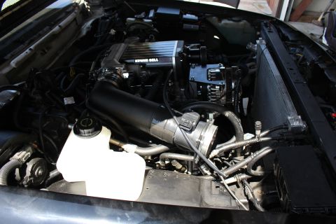 2003 Ford Crown Victoria - engine bay with a black intake tube feeding the supercharger, a coolant reservoir and radiator at the side.
