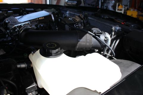 2003 Ford Crown Victoria - black intake tube arcing over a white coolant reservoir with a twist cap, near a Kenne Bell supercharger.