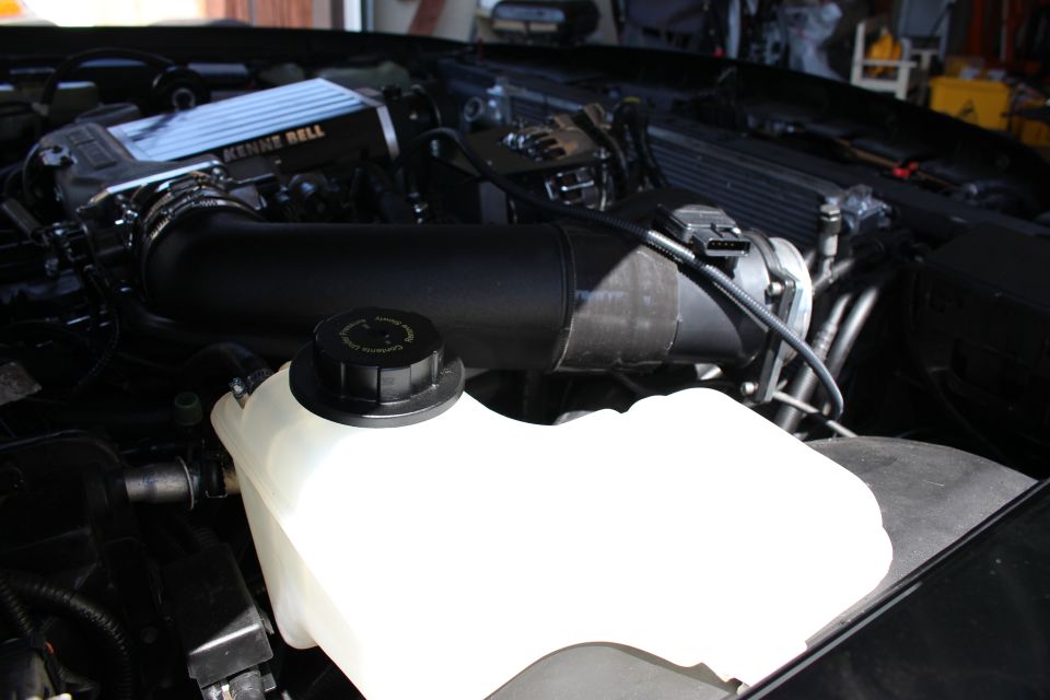 Black intake tube over a white coolant reservoir with twist cap