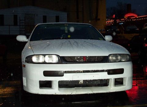 1998 Ford Crown Victoria - A white sports car is parked outside at night with lights reflecting on its wet surface.