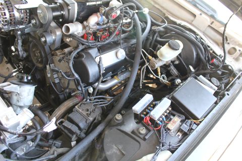 2003 Ford Crown Victoria - Under-hood view of a modified engine bay with visible wiring harness, brake master cylinder reservoir and an open fuse panel.