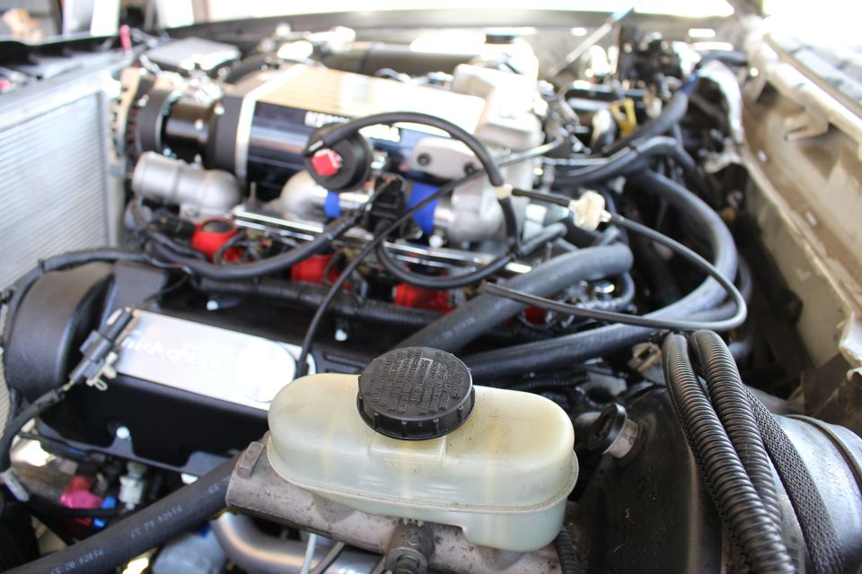 Close view of engine with supercharger, coolant reservoir and hoses